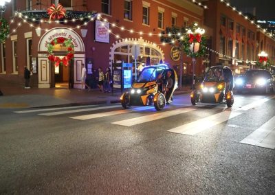 Night street scene with festive decorations, people, and unique three-wheeled vehicles.