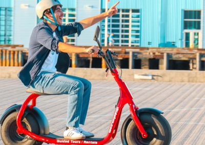 Person on a red electric scooter pointing in the distance, wearing a helmet and mask.