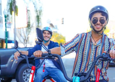 Two people riding electric scooters on a sunny urban street.