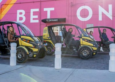 A yellow and black three-wheeled GoCar with two occupants on a colorful street.