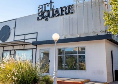 Exterior of 'Art Square' building with signage, lamp post, and greenery, under a clear sky.